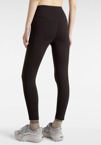 Svarta leggings med hög midja, texturerat material och kontrasterande sömmar. Matchas med ljusgrå sportskor och beige strumpor.