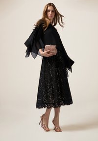 Schwarzes Spitzenkleid mit ausgestellt, gewelltem Saum; sheer schwarzer Schal; metallisch rose-goldfarbige Clutch; sandalenartige rose-goldfarbige Absätze.