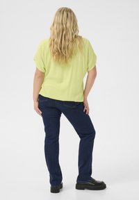 Limegrøn kortærmet top med tekstureret stof, parret med mørkeblå denimjeans og sorte platformssko. Håret er løst bølget.