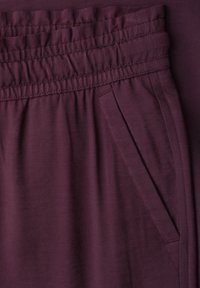 Pantalon à taille élastique violet foncé avec poche fendue latérale, coutures visibles et texture de tissu douce.