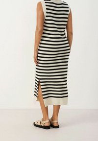 Ärmelloses gestreiftes Kleid in Schwarz und Creme mit gerippter Textur und seitlichen Schlitzen. Getragen mit beigefarbenen Sandalen mit Kreuzriemen.