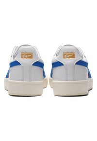 Białe skórzane sneakersy z niebieskimi tekstylnymi akcentami; posiadają brązową naszywkę z logo, wyściełany kołnierz oraz gumową podeszwę; prosty design i klasyczny kształt.