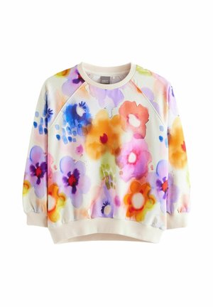 Barn iført en farverig sweatshirt med blomster, blå plisseret nederdel og glitrende høje sneakers med lilla snørebånd, stående på en ensfarvet baggrund.