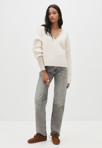 Beżowy sweter z dekoltem w serek i oversize'owymi rękawami, zestawiony z szarymi, nakrapianymi dżinsami. Brązowe buty w stylu mokasynów. Prosta, fakturowana tkanina.