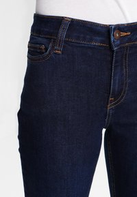 Dunkelblaue Jeans im Slim-Fit, mit vorderen Taschen, gestickten Details und einem einzelnen Metallknopf am Bund.