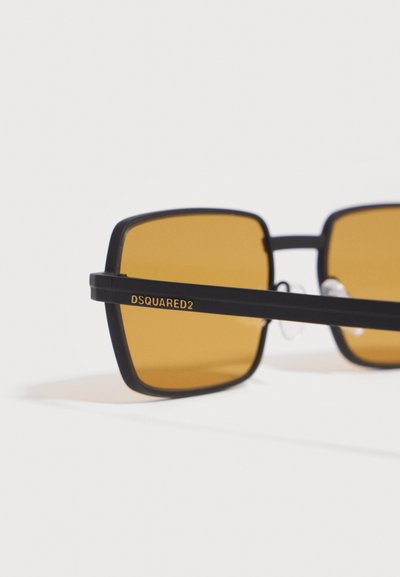 Lunettes de soleil rectangulaires noires avec verres orange et marquage "DSQUARED2" sur la branche, sur fond blanc uni.