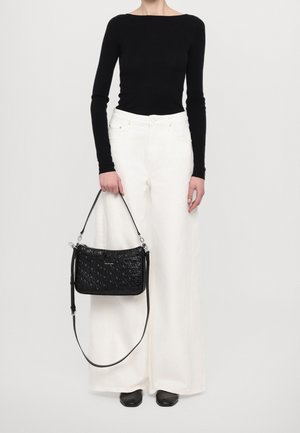 Black crossbody bag with a textured finish, silver hardware, and a detachable strap. Worn with white wide-leg pants and a fitted black top.