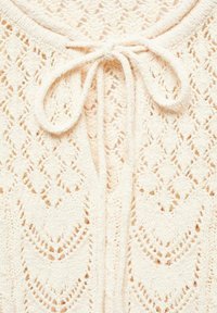 Crème-kleurig gebreid kledingstuk met een gemêleerd textuur, ronde halslijn en een striksluiting aan de voorkant.