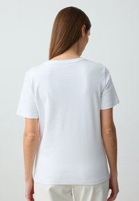 Maglietta bianca in cotone con collo rotondo e maniche corte, caratterizzata da una superficie liscia e un design semplice, vista da dietro.