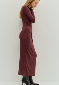 Sukienka z dzianiny w kolorze bordowym, z długim rękawem i dopasowanym krojem, ozdobiona marszczeniami po bokach. Połączona z czarnymi wysokimi botkami na obcasie.