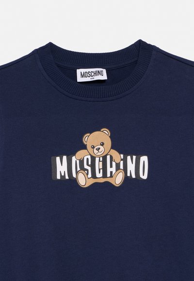 Marineblå barnegenser med ribbet rund hals, med en brun Teddybjørn-grafikk som holder "MOSCHINO"-logoen på brystet.