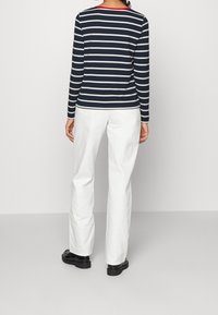 Marinblå och vit randig långärmad tröja med rund halsringning och röd accent. Matchad med vita raka byxor och svarta skor.