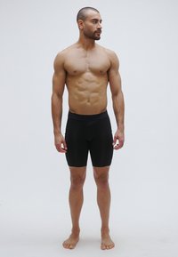 Μαύρο, εφαρμοστό αθλητικό σορτς από ελαστικό ύφασμα που φτάνει μέχρι τα μέσα του μηρού. Η ζώνη έχει ελαστική ταινία, με ομαλή υφή, χωρίς ορατά σχέδια ή λογότυπα.