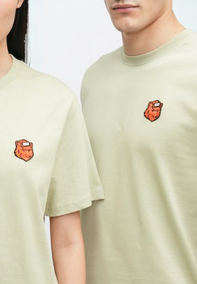 Svetlozelené bavlnené tričká majú na hrudi malé vyšívané oranžové hlavy medveďa. Krátke rukávy; uvoľnený strih.