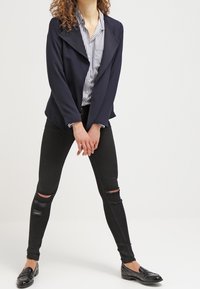 Námořnická sako s velkým límcem, pruhovaná košile, černé roztrhané skinny džíny a černé mokasíny. Hladká látka a volný střih.