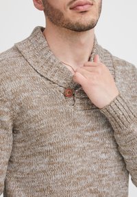 Strikket sweater i beige og creme nuancer, med en sjalkrave, en træknap og ribbede manchetter. Tekstureret mønster overalt.