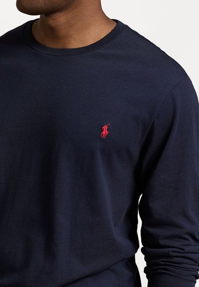 Marineblauw longsleeve t-shirt van katoen, met een ronde hals en een klein rood borduurlogo op de linkerborst. Gladde textuur.