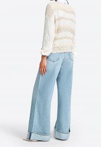 Rakennepintainen kerma- ja beige raidallinen neulepaita yhdistettynä leveälahkeisiin vaaleansinisiin farkkuihin, joissa on käännetty helma ja minimalistiset yksityiskohdat.