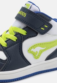 Youth sneaker featuring navy synthetic leather and white mesh panels, neon green accents, and a velcro strap. Textured rubber sole.