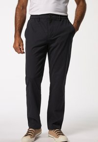 Granatowe chinosy o luźnym kroju, z elastycznym paskiem w talii i dwiema bocznymi kieszeniami, zestawione z jasnobrązowymi sneakersami na sznurówki.