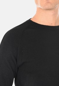 Maglione nero a maglia con scollo rotondo e colletto a coste. Presenta un design aderente e una texture liscia, con dettagli minimi.