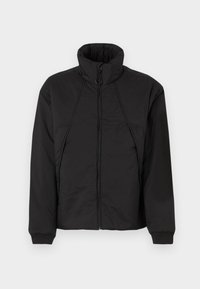 Veste rembourrée noire avec un col montant, une fermeture éclair et des poignets élastiques. Présente une texture légère et un design minimaliste.