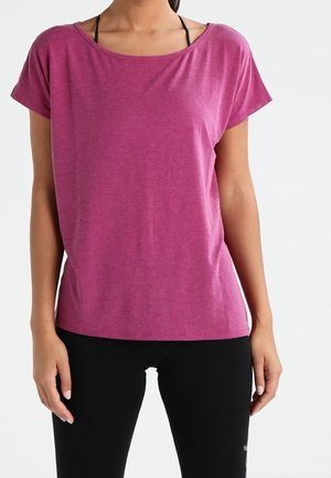 Vrouw draagt een loszittend, kort mouws magenta shirt over zwarte sportlegging, tegen een effen witte achtergrond.