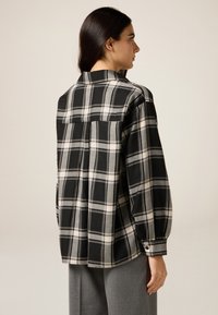 Svart och vit rutigt skjorta med långa ärmar, detaljerad ryggkropp och knäppte manschetter. Tillverkad av ett mjukt tyg.