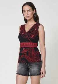 Top manica lunga nera con motivi floreali rossi e una fascia rossa strutturata in vita; abbinato a pantaloni corti in denim grigi con bordi decorati.
