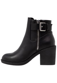 Bottine noire avec une texture en cuir lisse, fermeture éclair latérale, détail de boucle et talon empilé. Elle présente un bout arrondi et une semelle durable.