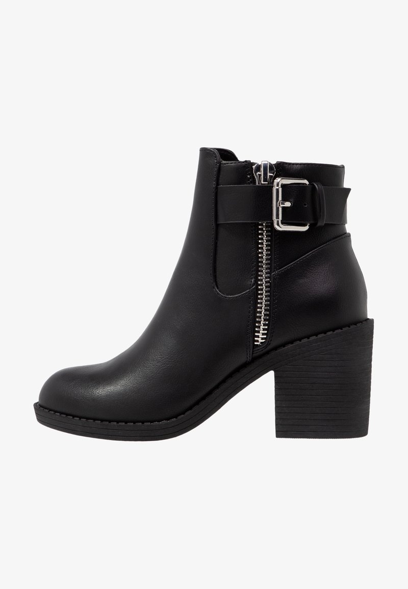 Bottine noire avec une texture en cuir lisse, fermeture éclair latérale, détail de boucle et talon empilé. Elle présente un bout arrondi et une semelle durable.