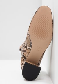 Botín de tacón con estampado de serpiente en tonos marrón y beige. Presenta un cierre de cremallera, parte superior texturizada y suela de goma negra sólida.