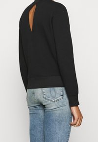 Schwarzer Sweatshirt mit einem Schlüssellochausschnitt auf der Rückseite, gerippten Bündchen und Saum, kombiniert mit hellblauen eng anliegenden Jeans. Material aus Baumwollmischung.