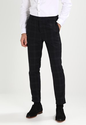 Zwarte geruite broek van een gladde stof, met een slim fit ontwerp, zijzakken en een knoopsluiting. Gemaakt met zwarte schoenen.