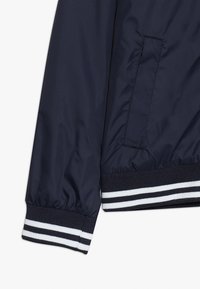 Giacca bomber blu navy con polsini elastici, dotata di tasca laterale e orlo a coste a righe in bianco e blu navy. Tessuto morbido e leggero.