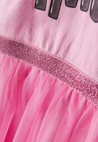 Rosa Kleid mit einem oberen Teil aus weicher Baumwolle, einem glitzernden rosa Taillenbund und einer Tüllrockschicht, die eine transparente, strukturierte Oberfläche zeigt.