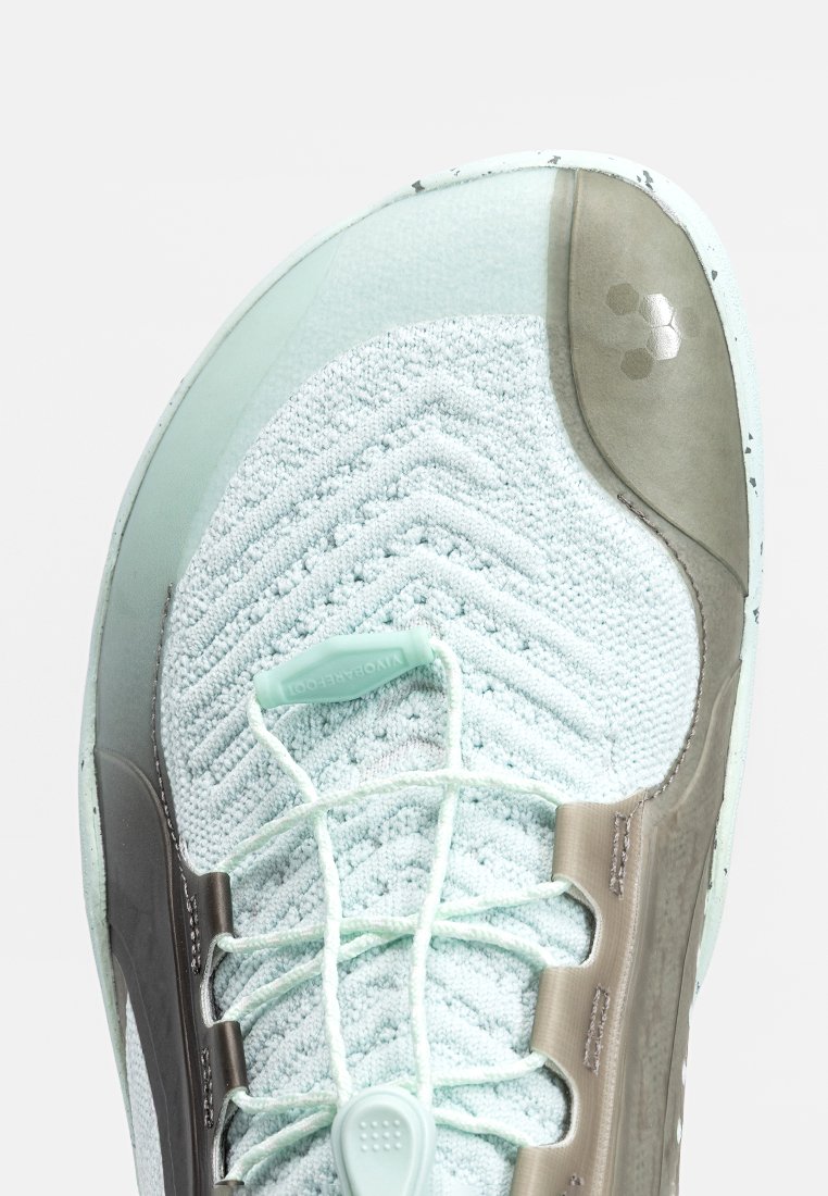 Acercamiento a una zapatilla de punto de color azul claro con cordones verde pálido y ojetes de plástico, que presenta patrones texturizados y una puntera de goma.