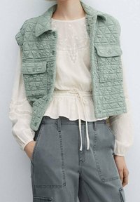 Gilet trapuntato verde menta con alette sulle spalle e tasche frontali, indossato sopra una blusa loose color avorio con dettagli testurizzati e vita con coulisse.
