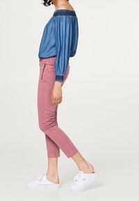 Top in denim con scollo off-the-shoulder e colletto arricciato, abbinato a pantaloni rosa a vita alta e sneakers bianche con fiocchi.