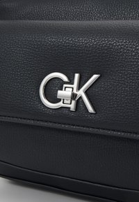 Schwarze, strukturierte Lederhandtasche mit einem auffälligen silbernen Logo-Verschluss, strenger Form und subtilen Nähdetails.