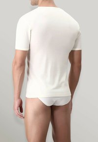 Maglietta bianca a maniche corte con scollatura rotonda, texture liscia e silhouette aderente, indossata con slip bianchi, su uno sfondo chiaro.