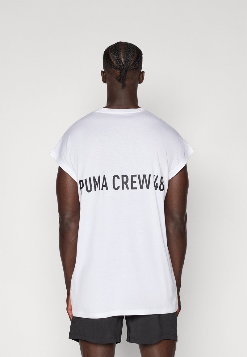 T-shirt blanc à manches courtes avec le texte noir "PUMA CREW '48" au dos. Le tissu semble doux avec une légère texture. Associé à un short noir.