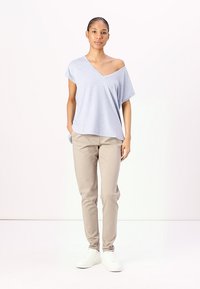 Maglietta oversize grigia chiara con scollatura a V e vestibilità comoda. Abbinata a pantaloni beige slim-fit e sneakers bianche. Texture liscia.