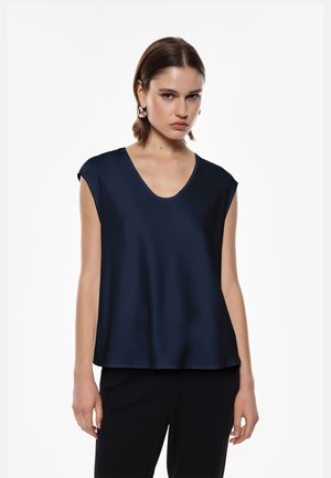Top in satin blu navy con scollo a V ampio, maniche a cappuccio e una vestibilità comoda, abbinato a pantaloni neri. Il tessuto ha una texture liscia e lucida.