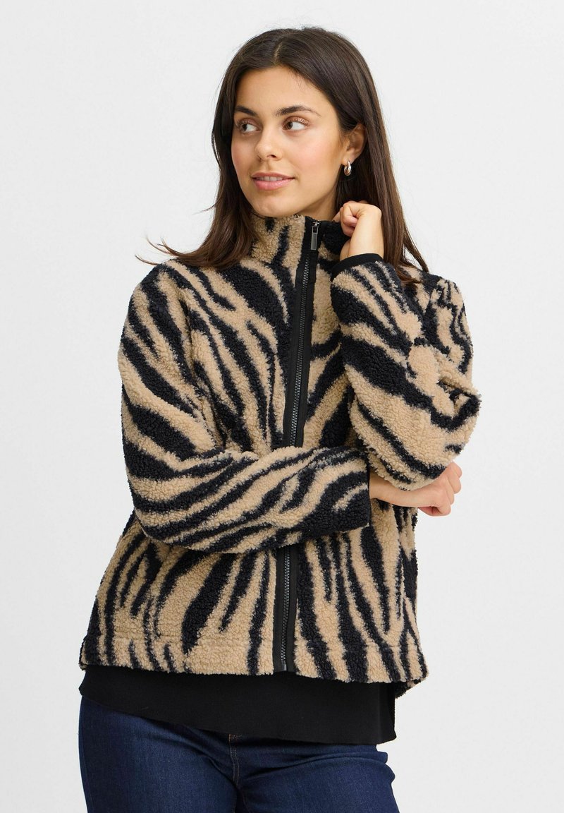 Veste en polaire rayée beige et noire avec un col montant et une fermeture éclair complète, dotée d'un tissu doux et texturé ainsi que de poignets élastiques.
