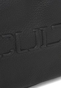 Borsa in pelle nera con superficie texturizzata e lettere in rilievo. Il design è minimalista, senza hardware o accenti visibili.