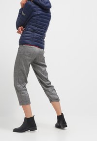 Granatowa puchowa kurtka z kapturem, szare ściągane spodnie i czarne botki za kostkę. Kurtka ma pikowaną teksturę i detal z logo.