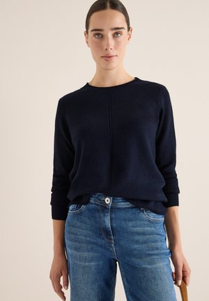 Marineblaues Strickpullover mit rundem Ausschnitt und gerippten Bündchen, kombiniert mit hellblauen Jeans aus Denim mit vorderen Taschen und Knopfverschluss.
