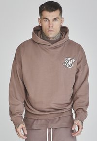 Sudadera marrón hecha de una tela suave y ligera. Cuenta con un bolsillo delantero, puños acanalados y un logo bordado en el lado izquierdo del pecho.