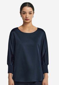 Granatowy satynowy top z szerokim dekoltem, długimi bufkami i luźnym krojem. Gładka faktura z delikatnym połyskiem oraz elastycznymi mankietami.